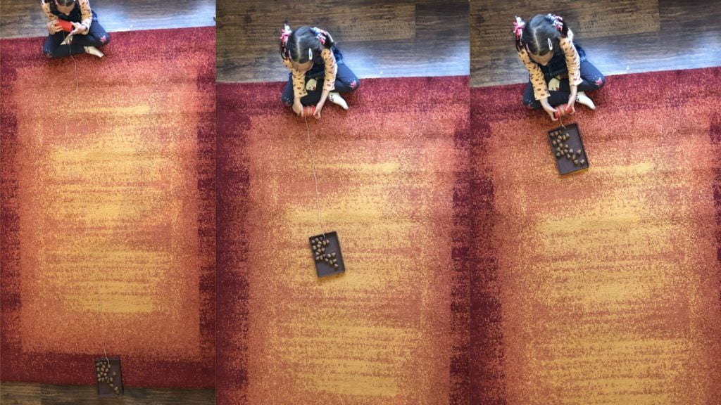 kislány cipősdoboz tetejéből készített tutajon makkokat húz át a szőnyegen