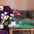 szék leterítve pléddel, rajta sokféle papír virág fajtánként szétválogatva, mellette zöld kis asztalon cserepes papírnövény, papír gyöngyvirág kosárban, egy örökcsokor