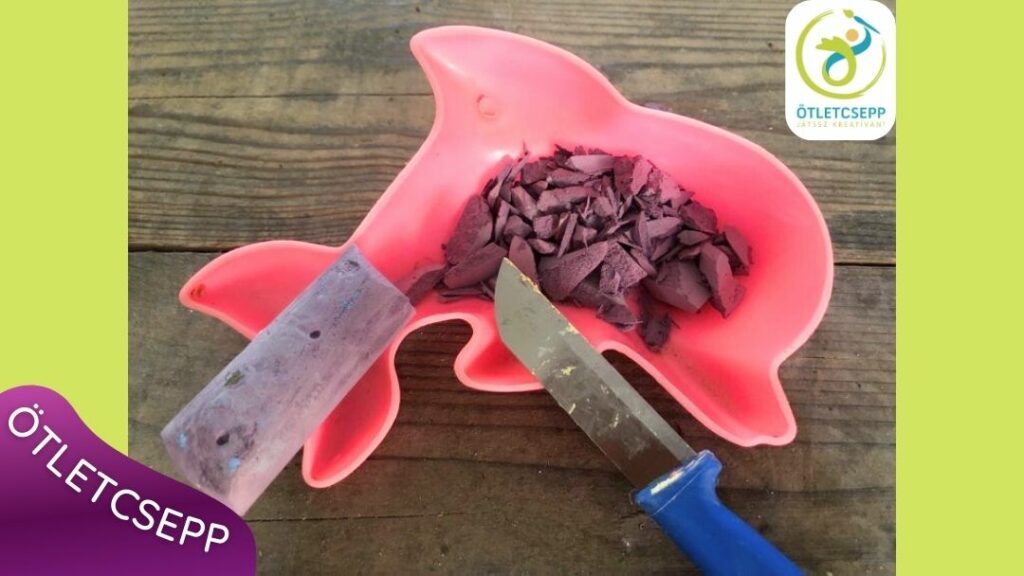 delfin homokozóformában lila krétaforgács, mellette lila kréta és egy kés