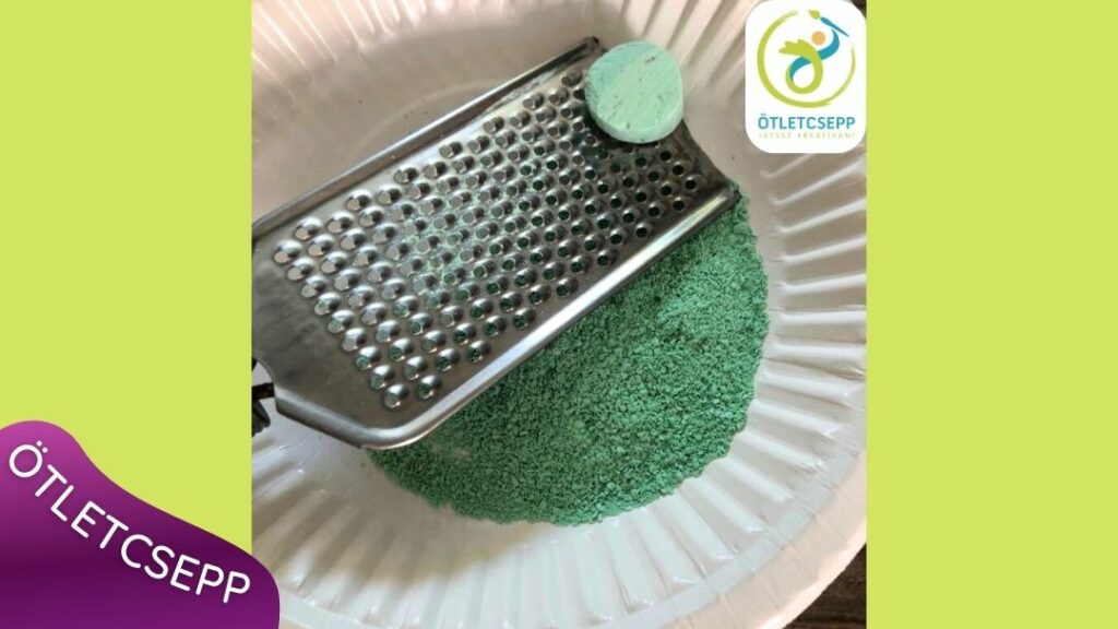 fehér papírtányéron zöld krétapor, felette egy kéz sajtreszelőn krétát reszel