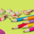 ötletcsepp logó, almazöld háttér előtt néhány színes ceruza és a belőlük lefaragott darabok
